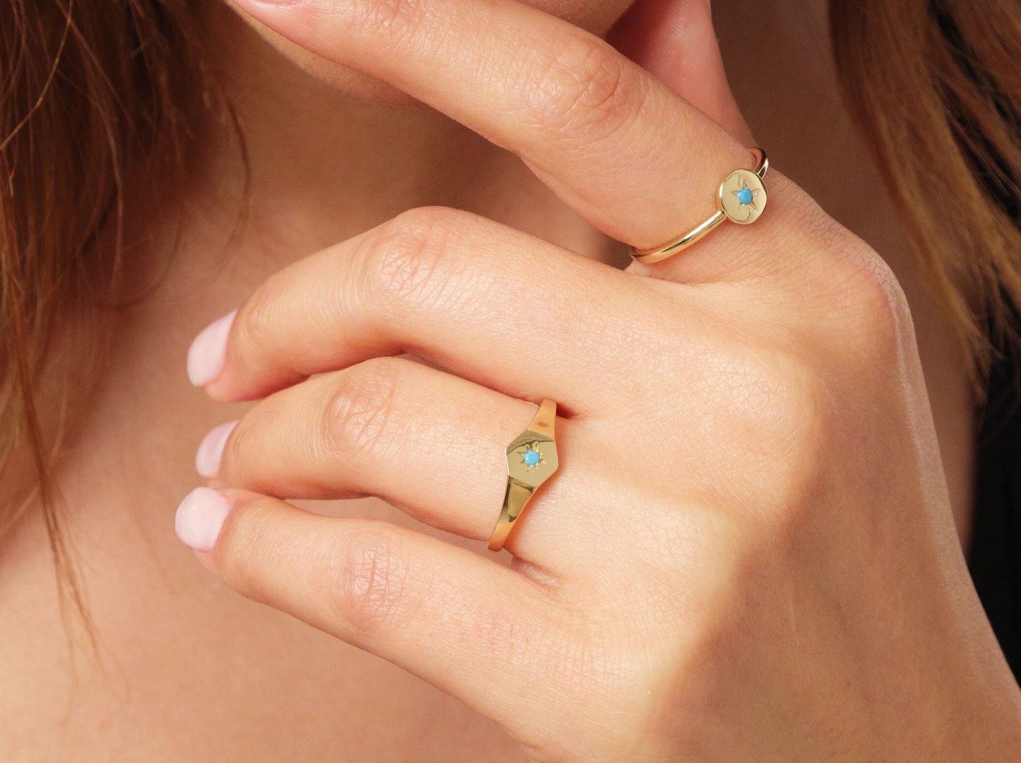 May include: Gold rings with turquoise starburst designs. One ring features a round face, while the other has a hexagonal face. The rings are worn on a hand with a light skin tone.