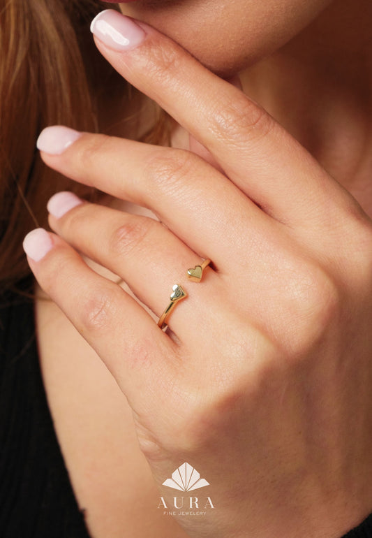 May include: Gold ring with two heart-shaped accents. The ring is open and adjustable. The ring is on a person's finger.