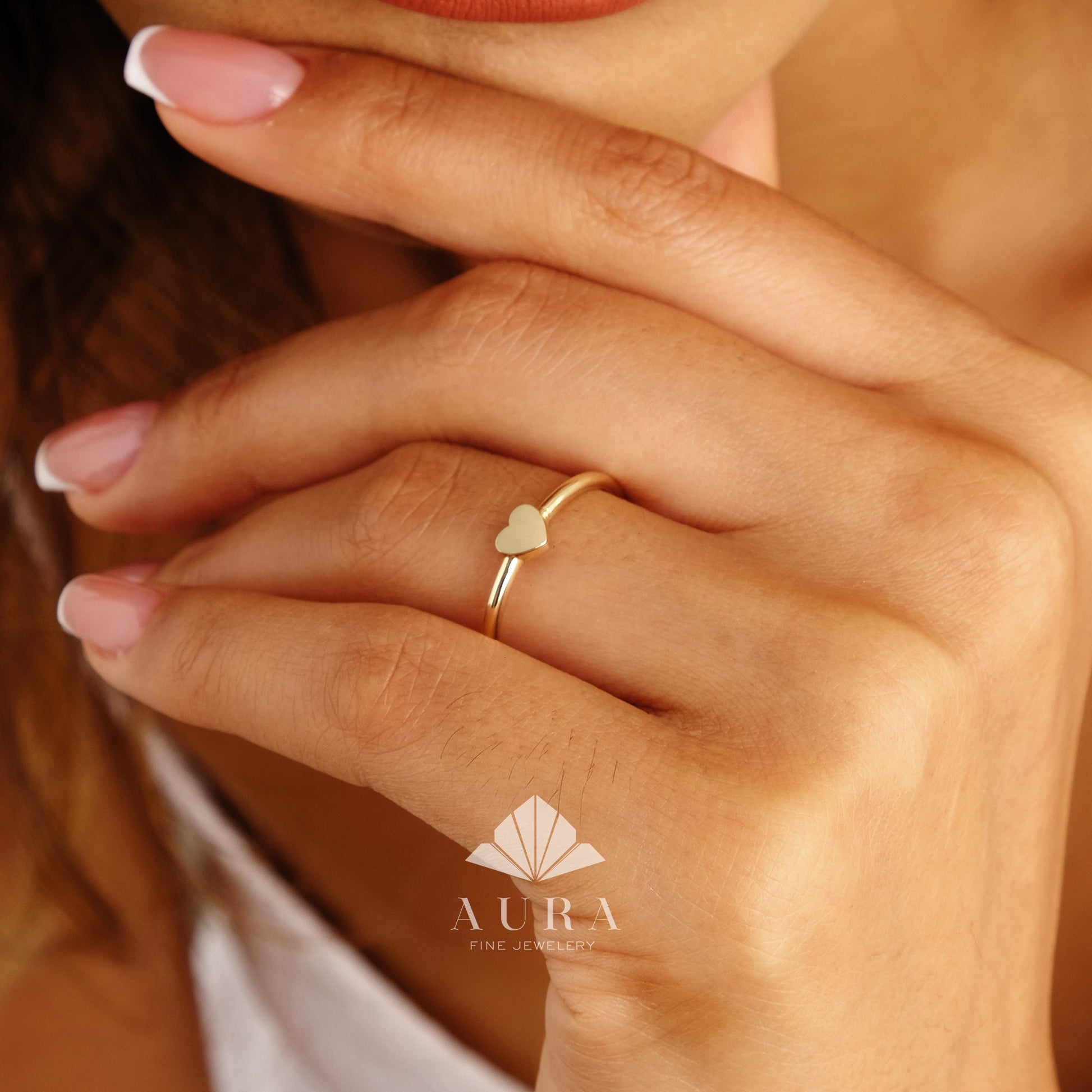 May include: A simple gold ring with a small heart-shaped design. The ring is worn on a person's finger.