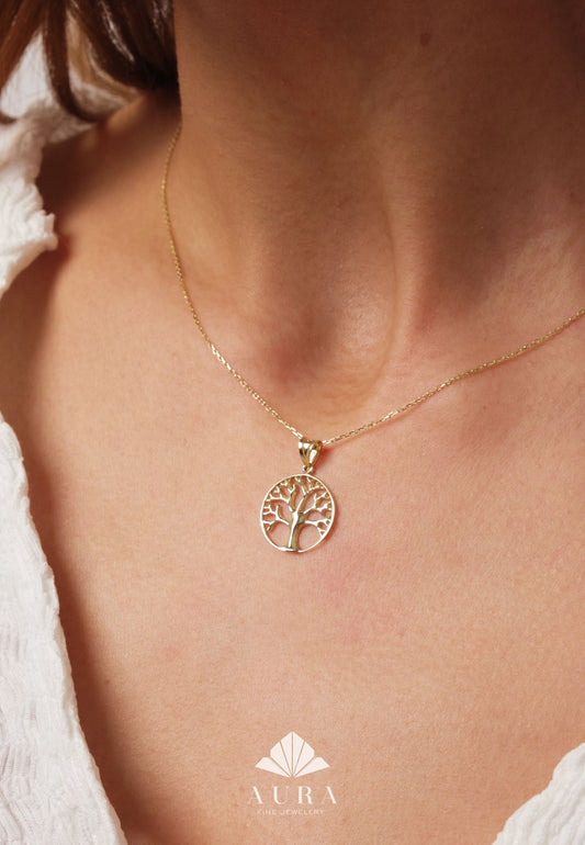 May include: A gold chain necklace with a delicate tree of life pendant. The pendant is circular and features a detailed design of a tree with branches and leaves.