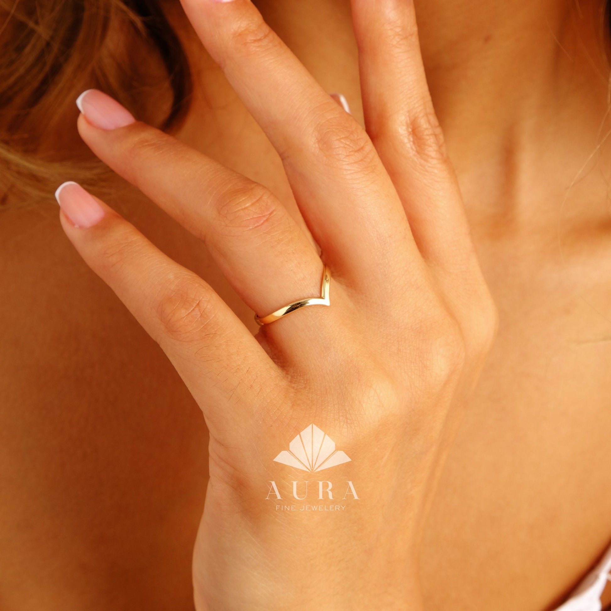 May include: A gold-colored V-shaped ring on a finger. The ring is simple and minimalist in design.