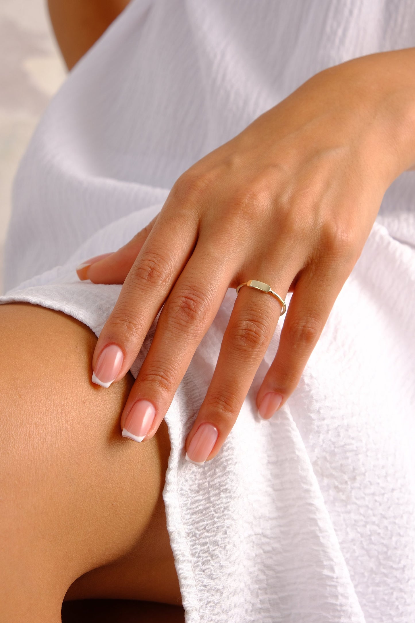 May include: A close-up of a hand wearing a thin gold band ring. The hand has a light skin tone and white french manicured nails.