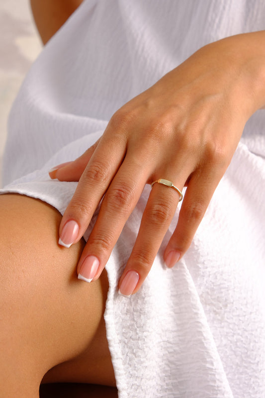 May include: A close-up of a hand wearing a thin gold band ring. The hand has a light skin tone and white french manicured nails.