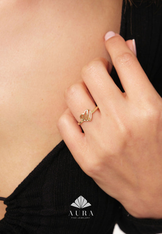May include: A gold ring with a delicate heart design. The ring is worn on a finger of a hand.