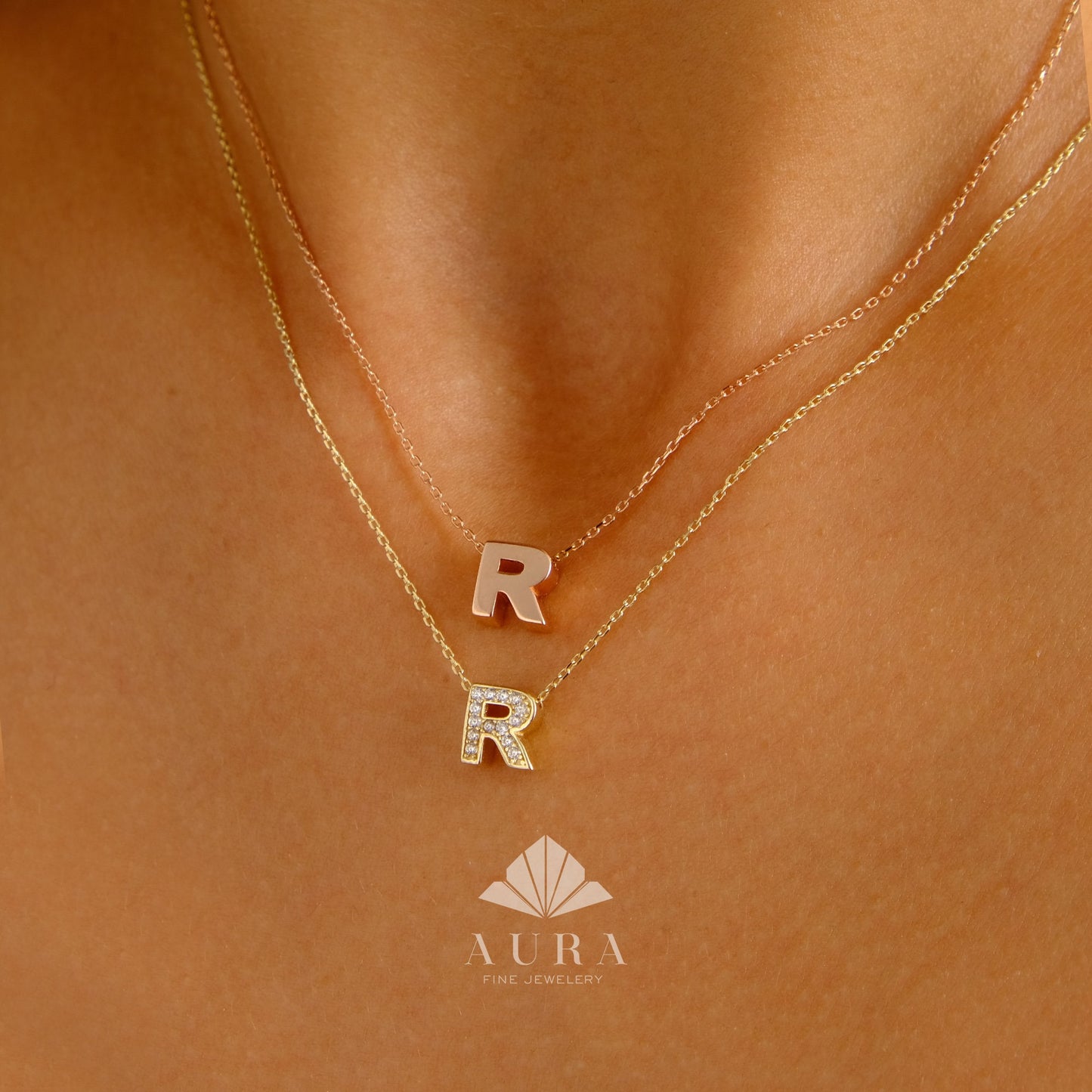 May include: Two gold necklaces with initial pendants. The top necklace has a plain gold 'R' pendant. The bottom necklace has a diamond-encrusted 'R' pendant. The necklaces are on a model's neck.