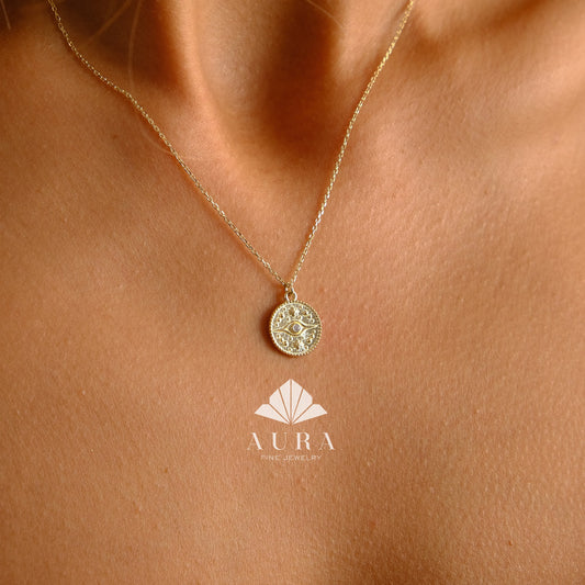 May include: A gold chain necklace with a round pendant featuring a detailed eye design. The pendant is surrounded by a circle of smaller stones. The necklace is on a model's chest.