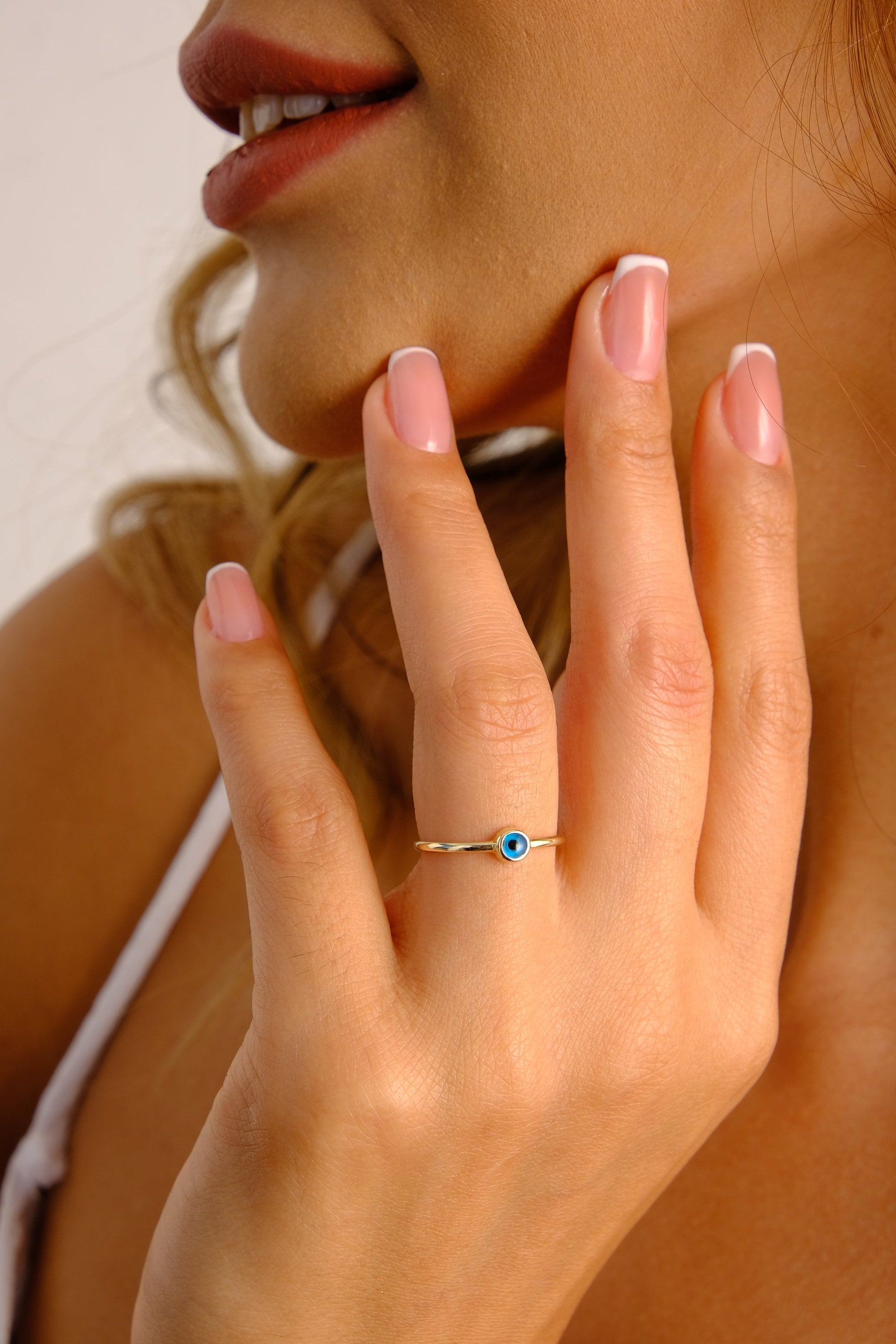 May include: A gold ring with a blue evil eye charm. The ring is on a person's finger.
