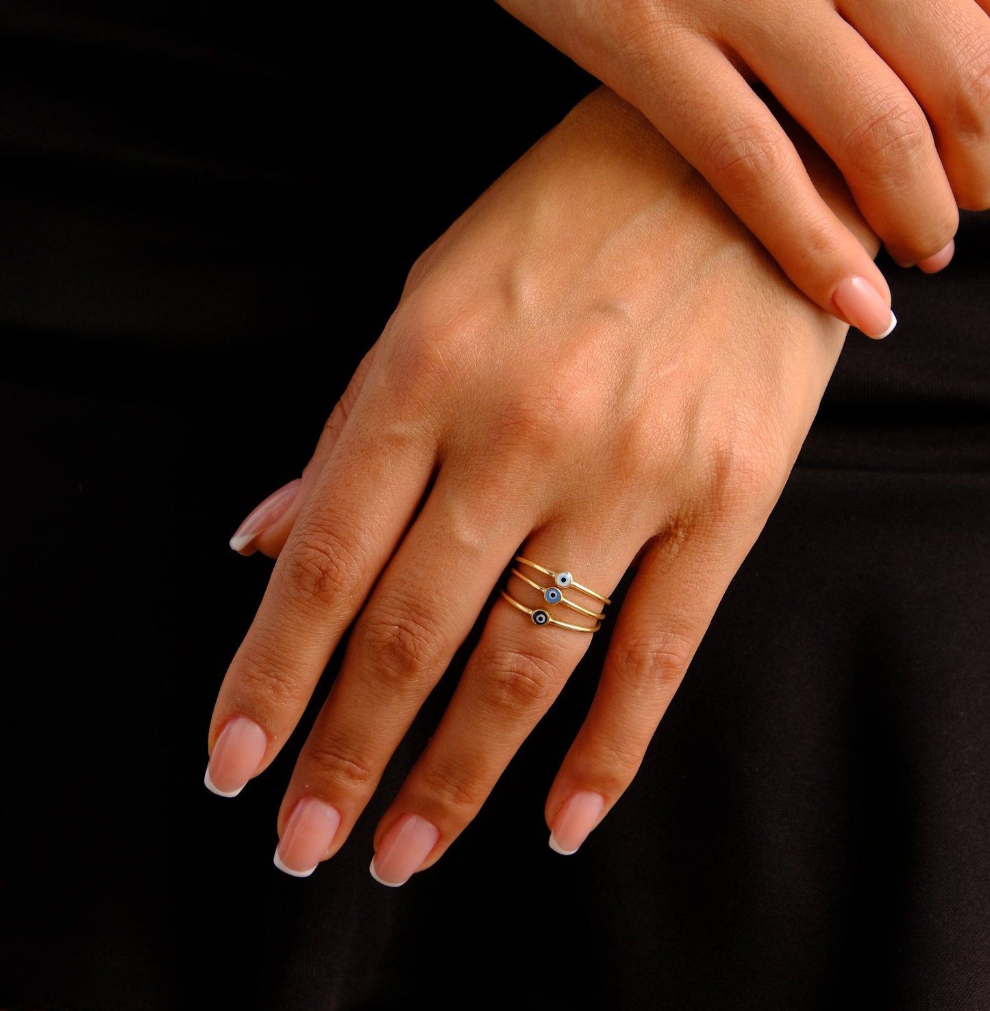 May include: Three gold rings with blue evil eye charms. The rings are stacked on a finger.