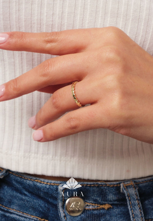 May include: A gold ring with a star design is worn on a finger. The ring is made of gold and features a series of small stars around the band. The person is wearing a white top and blue jeans. The ring is a piece of jewelry.