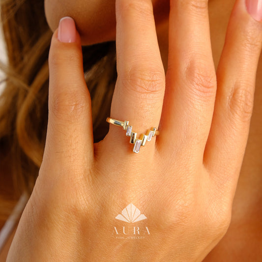 May include: A gold ring with a V-shaped design featuring baguette-cut diamonds. The ring is worn on a person's finger.